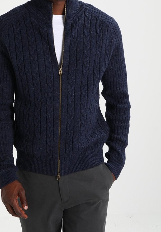 Marinblå kabelstickad cardigan med full dragkedja, ribbade muddar och nederkant, tillverkad av en texturerad ullblandning. Har en hög krage för extra värme.