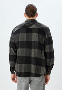 Koszula flanelowa w kratę w kolorze czarnym i szarym. Posiada luźny krój, prosty krój u dołu oraz mankiety zapinane na guziki. Miękka tekstura z casualowym designem.