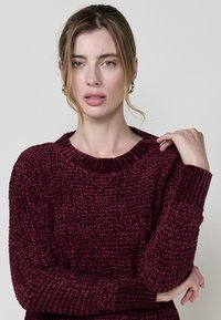 Burgunderfarbener, strukturierter Strickpullover mit geripptem Rundhalsausschnitt und umgeschlagenen Ärmeln. Bietet eine lockere Passform und ein weiches, gemütliches Material.