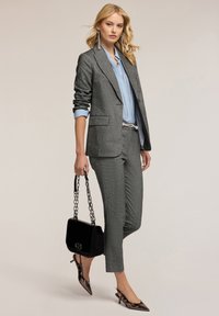 Szary garnitur skrojony na miarę z jasnoniebieską koszulą pod spodem. Posiada eleganckie tekstury, dopasowany krój i szpilki na patentowym obcasie w kształcie spiczastym. Dodatkowy element: czarna torebka.