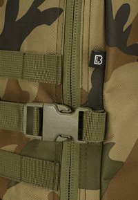 Zöld és barna árnyalatokban camouflázs mintás hátizsák anyag, műanyag csattal, cipzárral és megerősített varrással. Texturált felület.