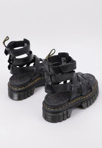 Sandalias de plataforma negras con correas anchas, suela texturizada y un tacón grueso y estriado. Incluyen una lengüeta en la parte trasera para facilitar el uso.