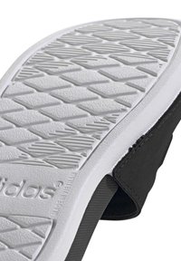 Svart slip-on sko med en texturerad gummisula. Sulan har ett mönstrat mönster och en präglad logotyp på sidan.