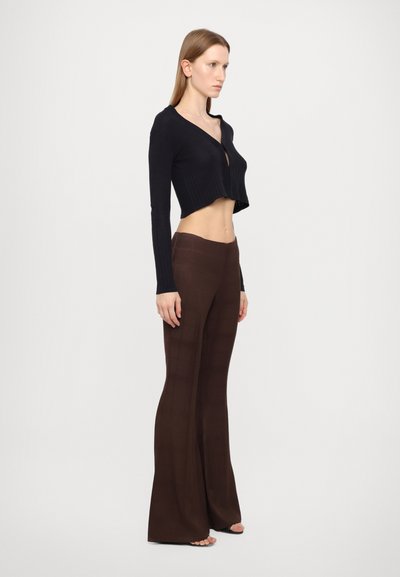 Black ribbed cropped cardigan with long sleeves, paired with brown flared pants featuring a smooth texture and subtle pattern details.