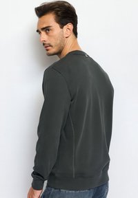 Felpa grigio scuro con scollatura tonda, tessuto testurizzato e dettagli di cucitura visibili lungo la cucitura laterale. Modello visto da dietro.