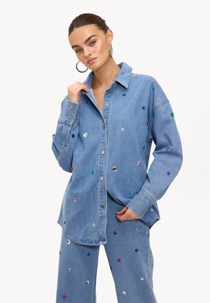 Chemise en denim ornée de pierres précieuses multicolores, avec un col pointu, des manches longues à poignets boutonnés et une coupe décontractée.
