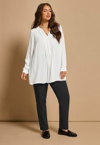 Blusa bianca a maniche lunghe con scollo a V, pieghe e pantaloni neri sartoriali abbinati a mocassini neri. Tessuto liscio, vestibilità comoda.