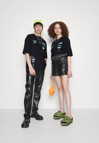 Černé grafické trička, kožené šortky a kalhoty. Neonově zelená kšiltovka, oranžová kabelka a černé oversized boty se zigzagovým vzorem.
