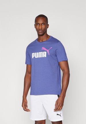 Lilla kortærmet t-shirt med stort hvidt "PUMA" logo og lyserødt accent. Har en klassisk rund hals og blødt bomuldsstof. Kan parres med hvide shorts.
