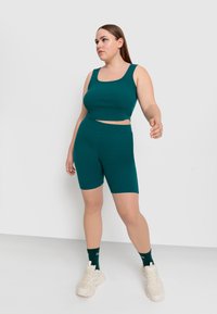 Set di top corto a coste color teal e pantaloni corti a vita alta. Tessuto morbido, design aderente, abbinato a sneakers chiare e calze scure.