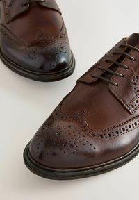 Chaussures en cuir marron à lacets avec un bout pointu, des détails brogue et une finition polie. Présente des perforations rondes et une semelle noire.