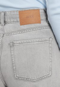 Γκρι τζιν από τζιν ύφασμα με καφέ δερμάτινο ένθετο με την επιγραφή "JJXX" στη μέση, διαθέτει διπλή ραφή και κλασικό σχέδιο πίσω τσέπης.