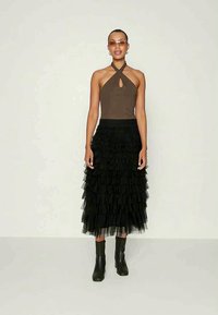 Brown halter top with a keyhole detail, paired with a black tiered tulle skirt and black ankle boots. Clear sunglasses complete the look.