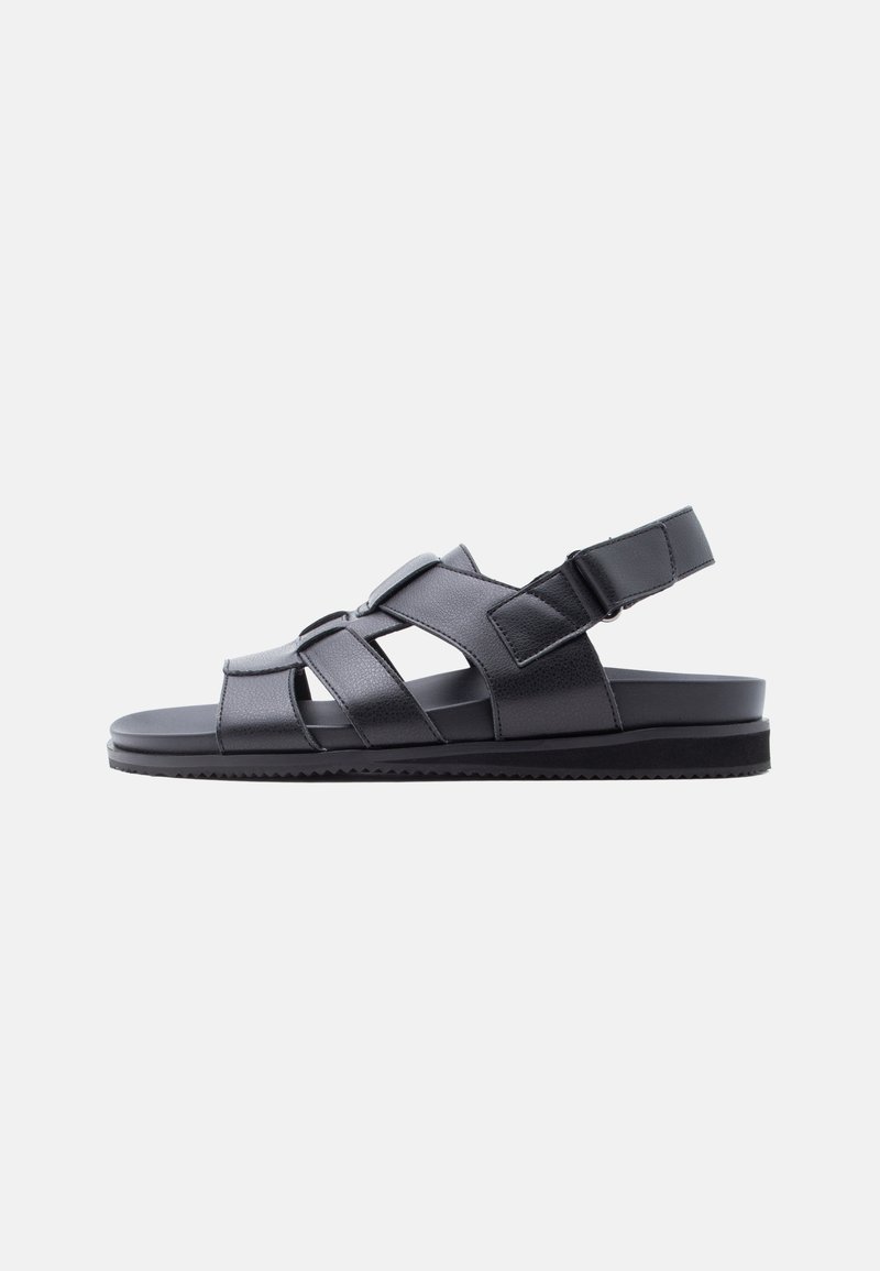 Sort lædersandal med flad sål, justerbare remme hen over foden og rundt om hælen samt lukket tåområde.