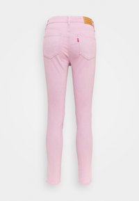 Jeans ajustados de color rosa claro vistos desde atrás, con dos bolsillos traseros, pasadores para cinturón y una etiqueta de cuero marrón de la marca en la cinturilla.
