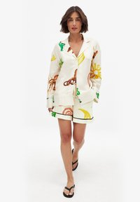 Vit pyjamaset med färgglada tryck av frukter och havsvarelser, korta ärmar, fickor och matchande shorts med svarta detaljer.