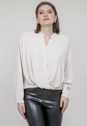 Chemisier crème à col mandarin, coupe décontractée, tissu texturé et ourlet noué, associé à un pantalon en cuir noir.