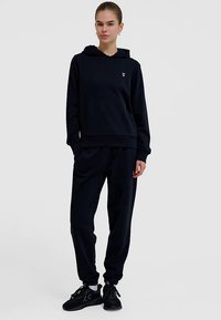 Marineblauer Pullover mit Kapuze und Fronttasche, kombiniert mit passenden Jogginghosen. Verfügt über ein minimalistisches weißes Logo auf der Brust und eine lockere Passform.