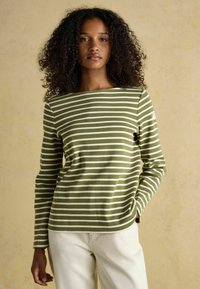 Roheline ja valge triibuline pika varrukaga särk, mis on valmistatud pehmest kangast, laia kaeluse ja lõdva istuvuse ning heledate pükstega.