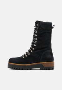 Stivali alla caviglia in suede neri con punta rotonda, chiusura con lacci, dettagli metallici e suola spessa marrone con un motivo di battistrada testurizzato.