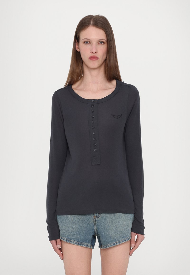Langärmliges dunkelgraues Henley-Shirt mit Rundhalsausschnitt, vorderer Knopfleiste und subtilen Logodetails, kombiniert mit Denim-Shorts.