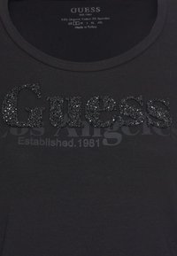 Zwarte t-shirt van 95% biologisch katoen en 5% spandex. Kenmerkt een glanzend, textuur 'Guess' logo in zwarte glitter met 'Los Angeles' erboven.