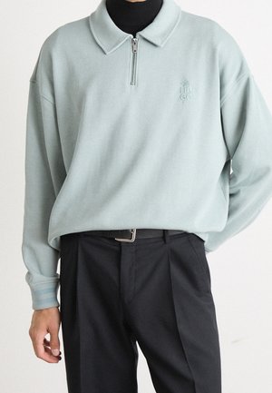 Helles grünes Pullover-Sweatshirt mit Kragen und Viertel-Reißverschluss. Verfügt über gerippte Ärmelabschlüsse und ein gesticktes Logo auf der Brust.
