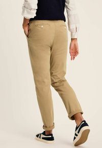 Khaki chinos with a tapered fit and rolled cuffs, featuring two back pockets with button closures. Paired with navy sneakers.