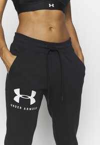 Schwarze Baumwoll-Jogginghosen mit elastischem Bund und Kordelzug. Mit einem großen weißen Under Armour-Logo am linken Bein.