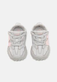 Gray sports shoes featuring a textured upper, pink accents, flexible design, and a cushioned sole, secured with standard laces and a heel tab.