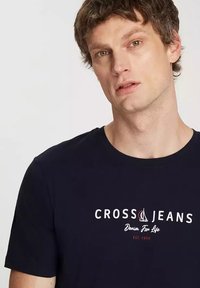 Granatowa bawełniana koszulka z logo "CROSS JEANS" i grafiką żaglówki w białym i czerwonym kolorze. Krótkie rękawy i okrągły dekolt. Luźny krój.