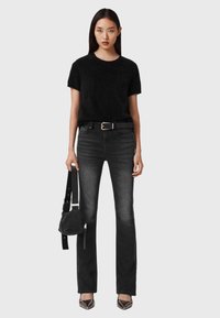 Zwart pluizig kortärmelig truitje gecombineerd met donkergrijze uitlopende spijkerbroek, zwarte riem, gestructureerde zwarte tas en puntige hakken met zilveren accenten.