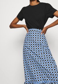 Schwarzes Oberteil mit Puffärmeln, kombiniert mit einem blau-schwarz karierten Rock mit einem gerafften Saum. Der Stoff ist glatt und hat eine figurbetonte Silhouette.