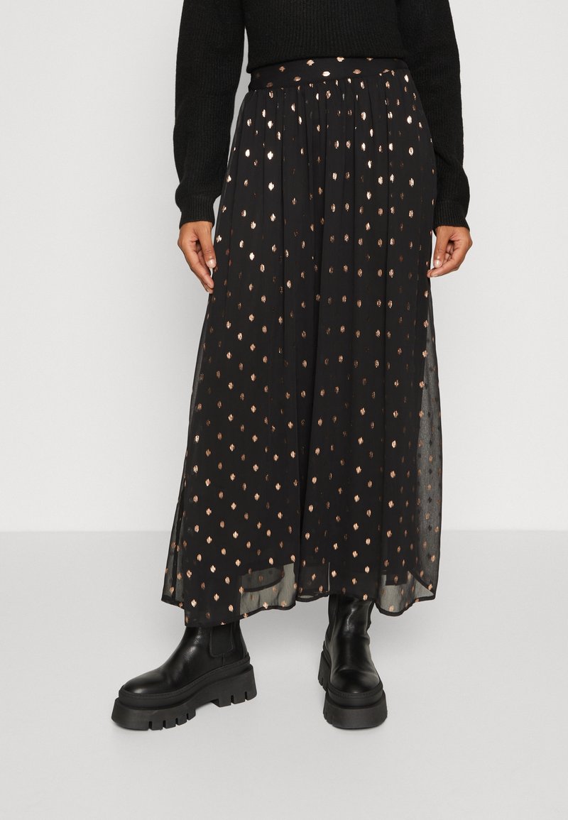 Jupe midi noire à pois dorés, associée à des bottes noires épaisses et un haut noir à manches longues, présentée de la taille jusqu'au sol.