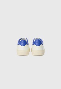Hvite sneaker med blå detaljer, glatt lær overdel, avrundet tå, flat kremfarget såle og pregemerkede detaljer på hælen. Rent og moderne design.