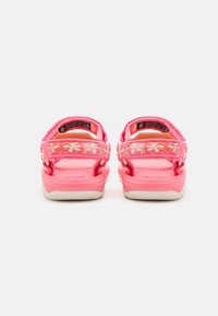 Un par de sandalias rosas para niños con correas ajustables de estampado floral y suelas blancas, vistas desde atrás sobre un fondo blanco.