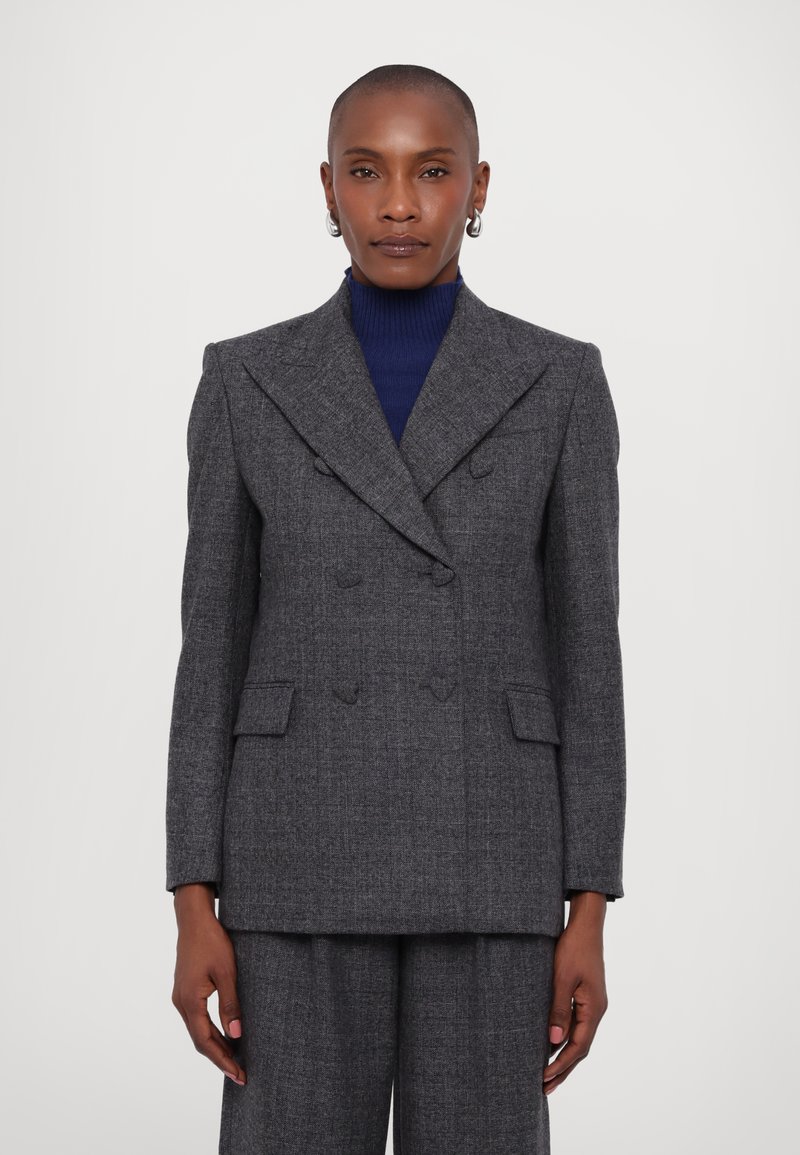 Blazer grigio doppiopetto con una vestibilità strutturata, caratterizzato da un tessuto testurizzato, reverse a punta e tasche frontali. Abbinato a un dolcevita blu navy.
