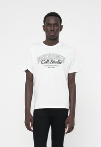 Λευκό βαμβακερό t-shirt με στρογγυλή λαιμόκοψη, κοντά μανίκια και εκτυπωμένο μαύρο κείμενο, συνδυασμένο με μαύρο παντελόνι.