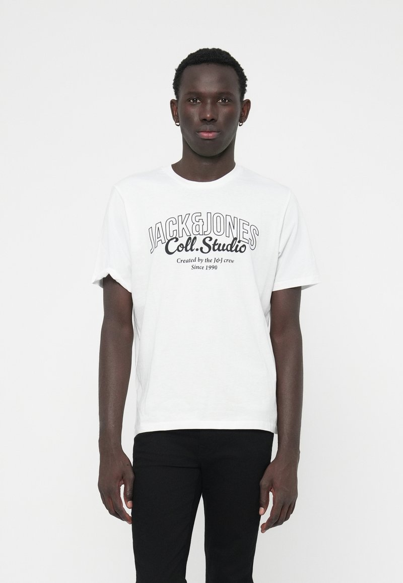 T-shirt en coton blanc avec un col rond, des manches courtes et un texte noir imprimé, associé à un pantalon noir.