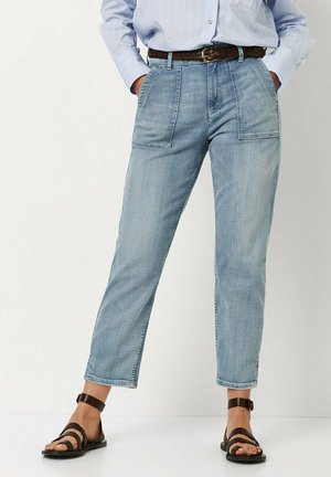 Hellblaue Jeanshose mit geradem Bein, ausgestattet mit zwei vorderen Taschen und einem hohen Bund. Kombiniert mit braunen Sandalen mit Riemchen.