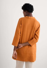 Roestkleurige linnen tuniek met driekwartmouwen, licht oversized pasvorm, kraagdetail en een gladde, gemêleerde afwerking.