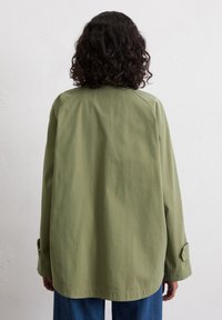 Olive green, lightweight, oversized jacket with long sleeves and buttoned cuffs. Smooth texture and simple design, viewed from the back.