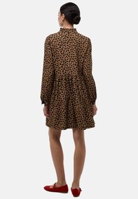 Robe à motif léopard brun avec des manches longues, une taille froncée et un col montant, associée à des ballerines rouges. Tissu lisse avec un design fluide.