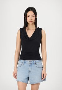 Zwarte mouwloze top met gedrapeerde halslijn, strakke pasvorm en geplooide textuur bij de taille, gecombineerd met lichtblauwe denim shorts.