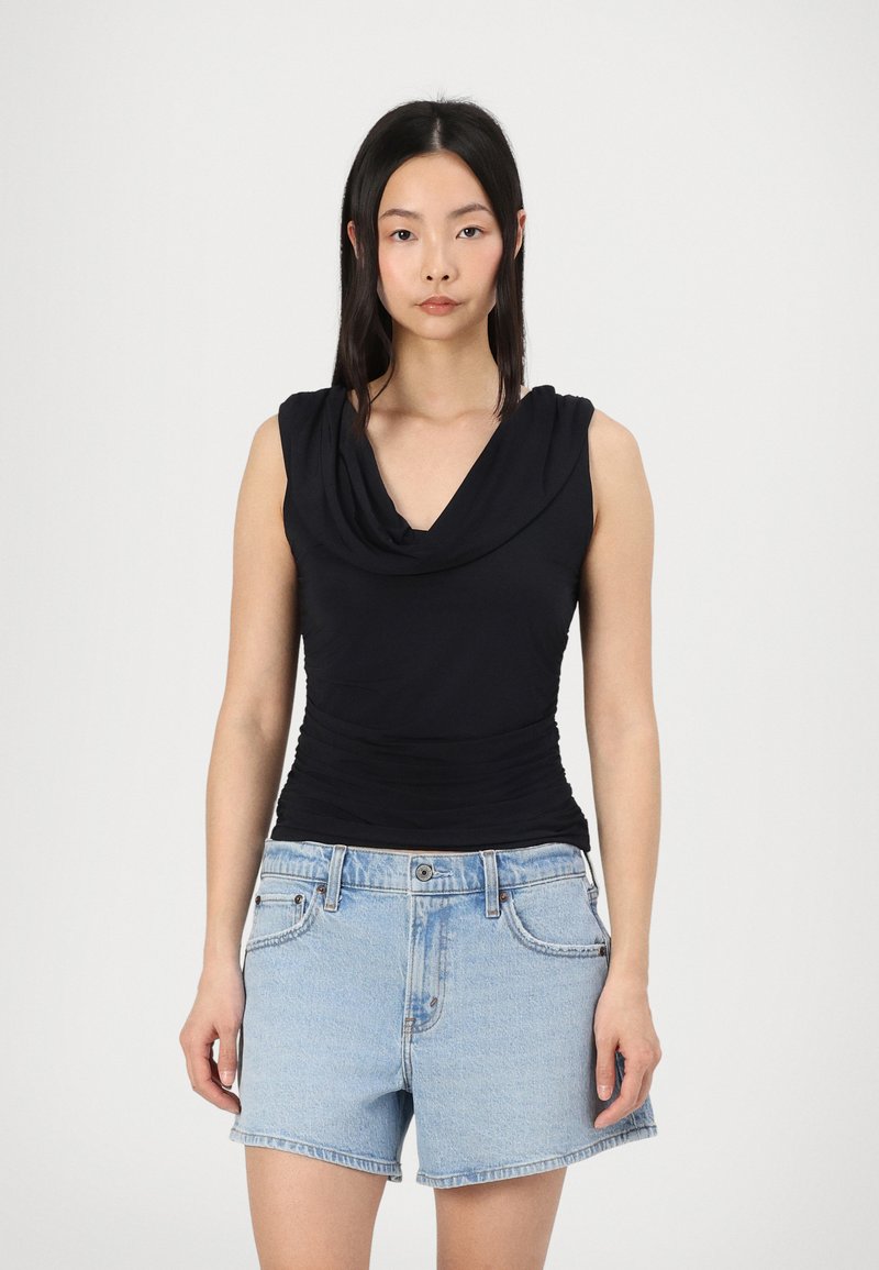 Zwarte mouwloze top met gedrapeerde halslijn, strakke pasvorm en geplooide textuur bij de taille, gecombineerd met lichtblauwe denim shorts.