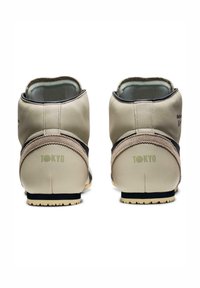 Beżowe skórzane botki za kostkę z ciemnobrązowym akcentem i teksturowanym obcasem. Na obcasie znajduje się zielona marka "TOKYO" oraz biała gumowa podeszwa.