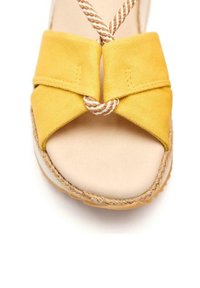 Sandalia espadrille de lona amarilla con un diseño de tira cruzada, acento de cuerda trenzada y una zona de punta redonda en tono marrón.