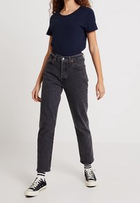 Mörkgrå högmidjade jeans med rak passform, kombinerat med en marinblå t-shirt och svarta sneakers. Midjelängd på uppviktningarna.