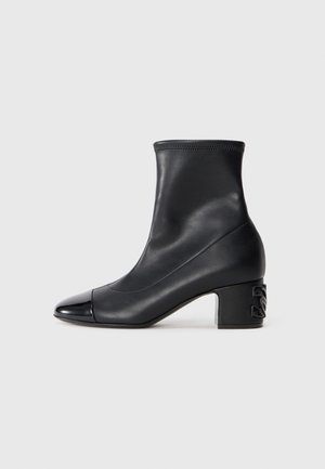 Botte en cuir noire mi-mollet avec un bout rond, talon bloc avec un détail décoratif embossé, et tige lisse sans couture.
