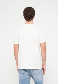 Balta īsrokšķkotne kokvilnas t-kreklam ar apaļu kaklu, vienkārša dizaina un brīva piegriezuma, redzama no aizmugures.